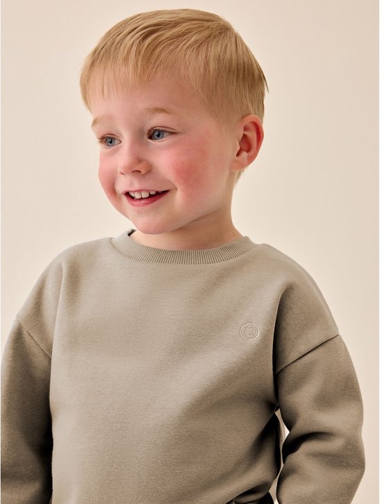 Close-up van een jongen in een naturelkleurige sweater met een geborduurd lachend gezichtje.