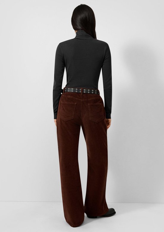 Achterkant van model in zwarte coltrui met lange mouwen en bruine ribfluwelen broek met riem.