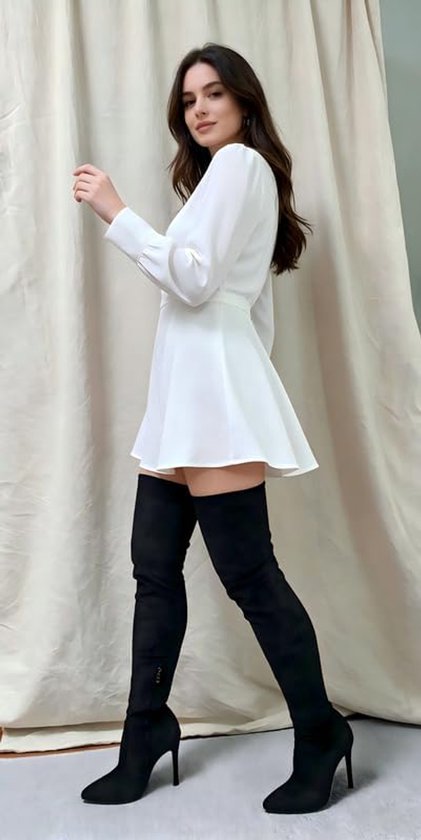 Model draagt een wit jurkje met lange mouwen en zwarte overknee-laarzen met naaldhak.