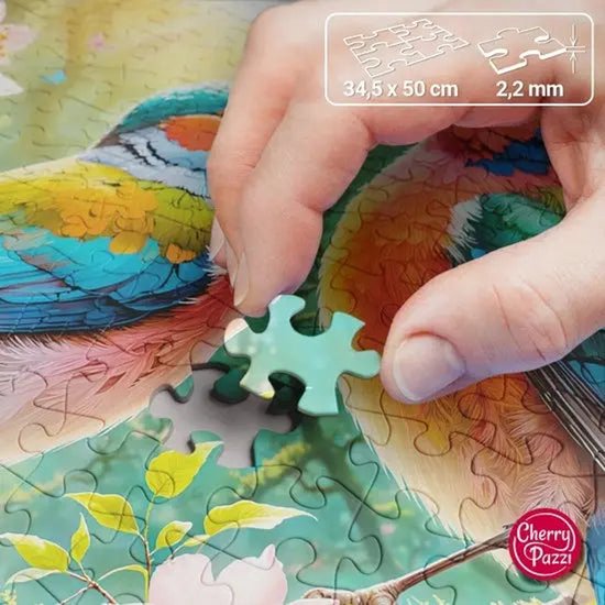 Hand die een lichtgroen puzzelstukje plaatst op een puzzel met kleurrijke vogels, bloemen en vlinders. Afmetingen 34,5 x 50 cm, 2,2 mm.