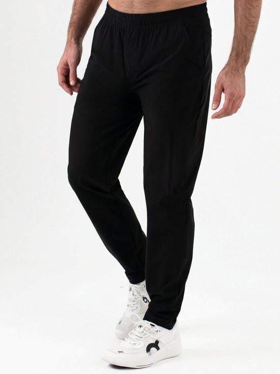Zijzicht van een man in een zwarte trainingsbroek en witte sneakers. Elastische tailleband.