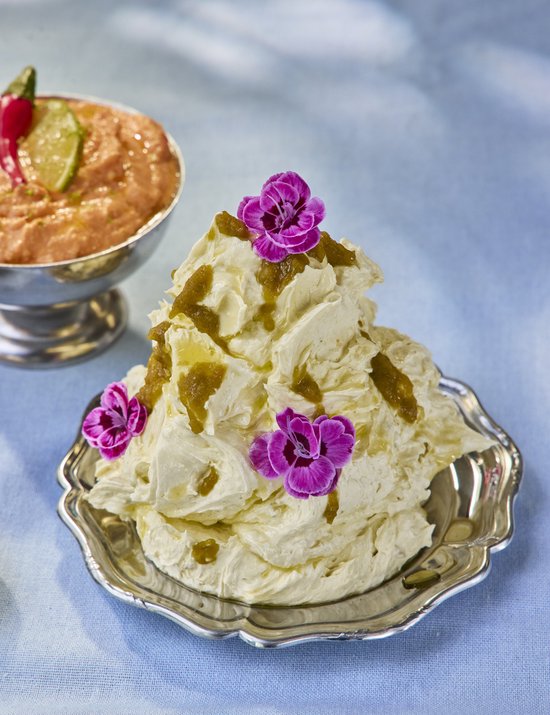 Luchtige room met olijfolie, groene chutney en paarse eetbare bloemen, geserveerd op een zilveren schaal.