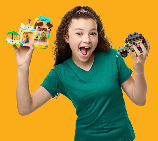 Fille aux cheveux bouclés en t-shirt vert tenant une animalerie rose et une jeep, toutes deux en LEGO.