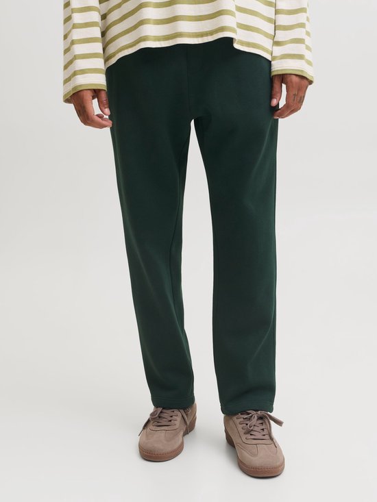 Onderlichaam van een man in een donkergroene joggingbroek en bruine sneakers.