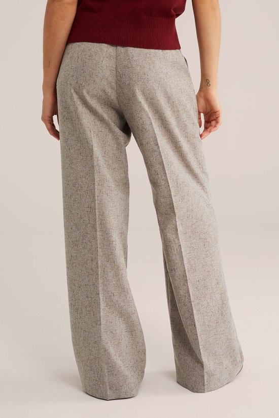 Model in een gemêleerde grijze wijde broek, zicht van achter.