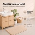 Beige badmat met zacht memory foam, naast een houten badkamermeubel.