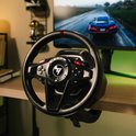Zwart racestuur met rode markering bovenop, bevestigd aan een bureau, met een computerscherm op de achtergrond.