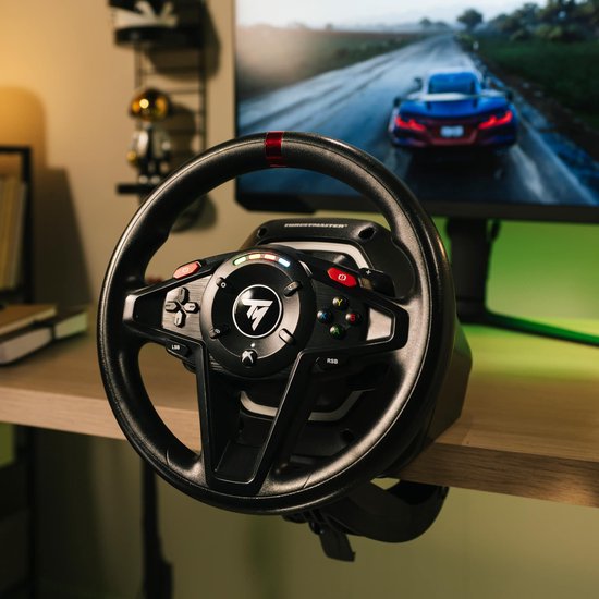 Zwart racestuur met rode markering bovenop, bevestigd aan een bureau, met een computerscherm op de achtergrond.