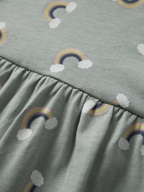 Close-up van een lichtgroene jurk met lange mouwen, de stof heeft een geribbelde textuur en is bedrukt met regenboogjes.