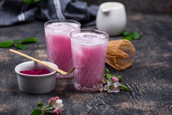 Twee glazen roze bietendrank met ijs en schuim, met een bietenschepje en bloesems.