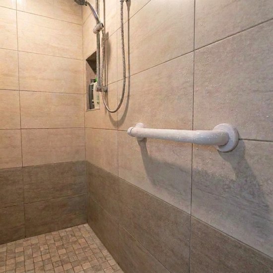 Witte handgreep met geribbelde grip gemonteerd op een betegelde douchewand.