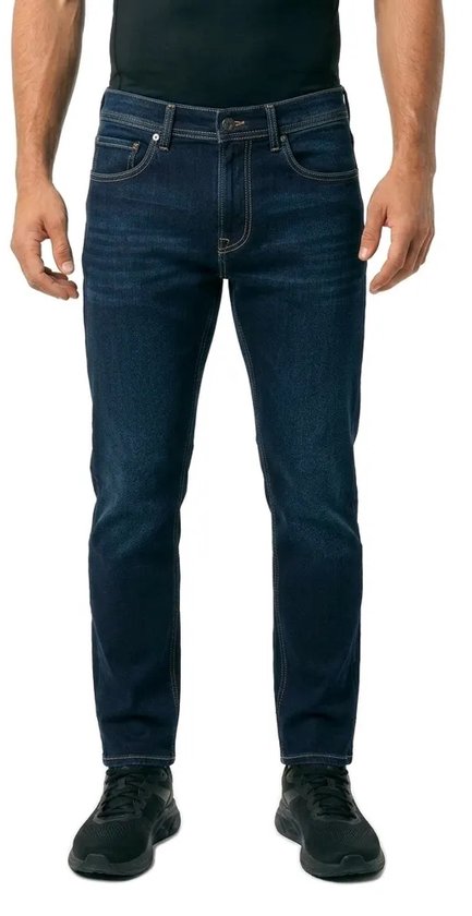 Man draagt een donkerblauwe slim fit spijkerbroek met gele stiksels en lichte slijtage op de bovenbenen.