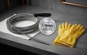 Furet argenté avec poignée noire et gants jaunes sur un plan de travail en béton. Comprend un logo circulaire argenté avec '3 Meter Nettoyeur de Drain Professionnel'.