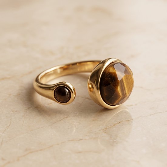 Gouden ring met grote facet geslepen tijgeroog en kleine ronde onyx op marmer.