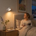 Oplaadbare, dimbare witte wandlamp verlicht een vrouw die in bed leest. Nachtlampje.
