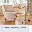 Verstelbare bedtafel met wielen naast een fauteuil, met een boek erop.