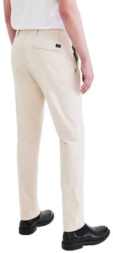 Man in beige chino broek met zwarte schoenen. Zichtbaar is de achterkant van de broek.