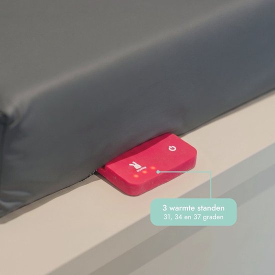 Close-up van een roze bedieningsknop met Wumby-logo en warmte-instellingen op een antraciet aankleedkussen.