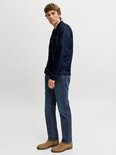 Zijaanzicht van een model in een donkerblauw denimjack en een medium blauwe jeans met suède laarzen.