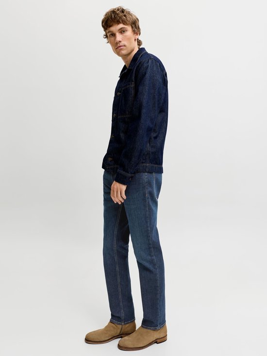 Zijaanzicht van een model in een donkerblauw denimjack en een medium blauwe jeans met suède laarzen.