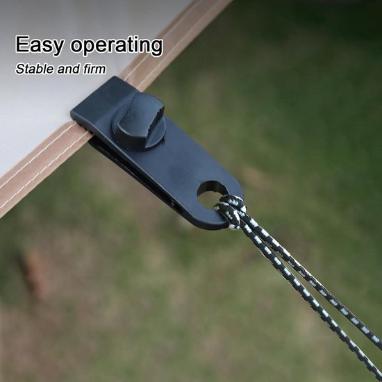 Zwarte tarpclip met klemmechanisme, bevestigd aan een beige luifel met bruine zoom. Een zwart-wit koord zit door de clip.