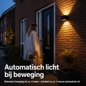 Vrouw met boodschappentassen bij een deur, verlicht door een automatische wandlamp.