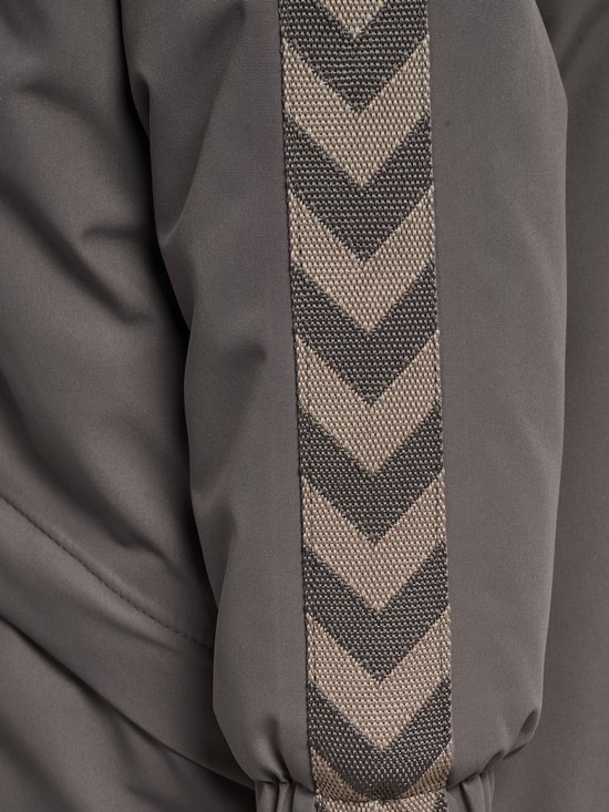 Detail van een donkergrijze jas met chevron-streep op de mouw.