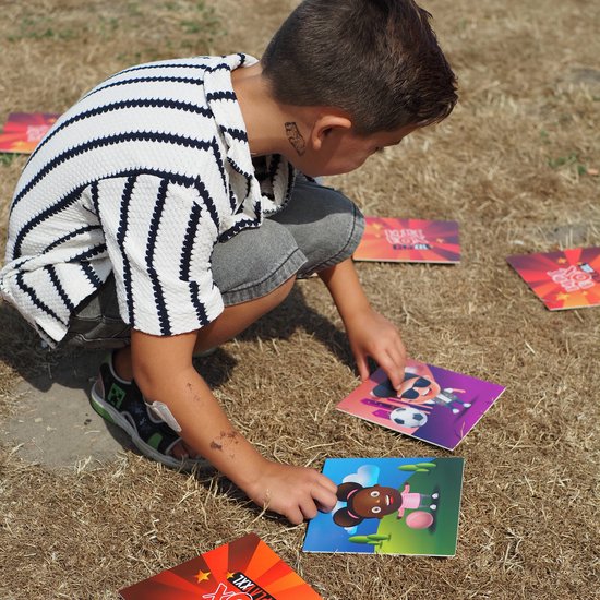 Jongen met gestreept shirt raapt kaarten met dierensymbolen op droog gras.