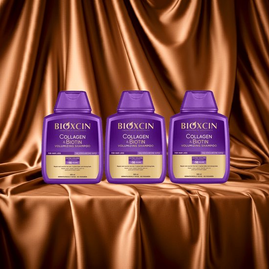 Drie paarse Bioxcin Collageen & Biotine Volume Shampoo flessen met gouden labels, op een bruine satijnen achtergrond.