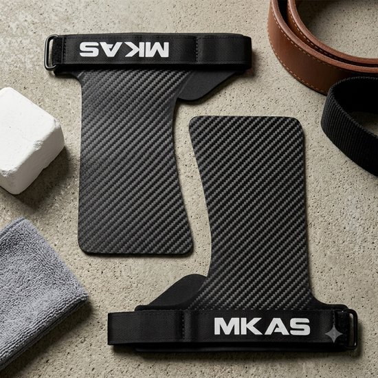 Zwarte handgrepen met "MKAS" erop, met een carbonfiber-textuur, naast een handdoek en een gewichthefriem.