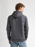 Achterkant van een man met krullend haar in een donkergrijs gemêleerd vest.