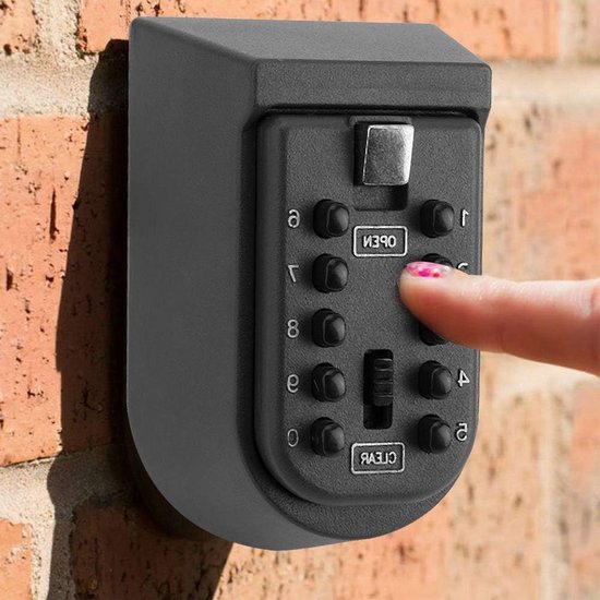 Hand die een zwarte metalen sleutelkluis op baksteen bedient. Vinger drukt cijfer 3 in.