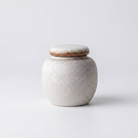 Kleine witte urn met cementlook en bruine rand op witte achtergrond.