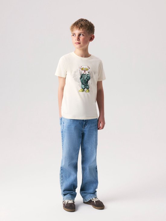 Jongen in crème T-shirt met grafische print en lichtblauwe spijkerbroek.
