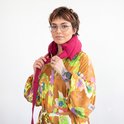 Vrouw met bril en kleurrijke jurk met bloemenprint, met rode warmtekussennekband.
