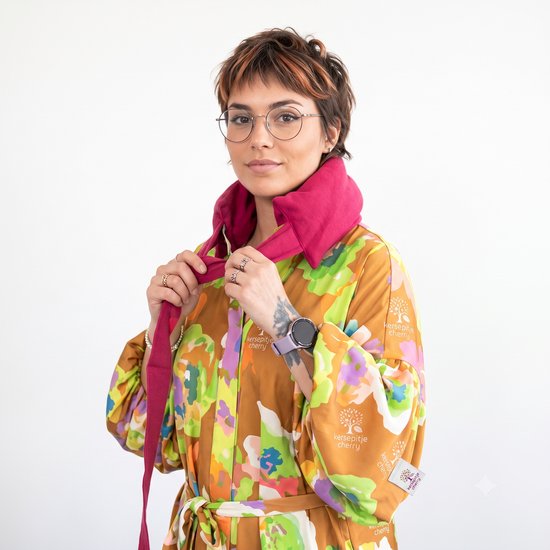 Vrouw met bril en kleurrijke jurk met bloemenprint, met rode warmtekussennekband.