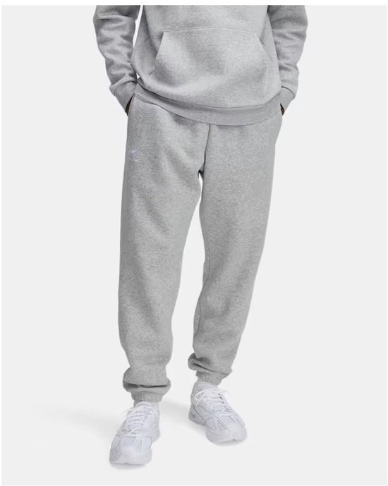 Grijze joggingbroek met kleine logo op de linker heup, op een model met witte schoenen.