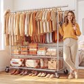 Een vrouw met een oranje trui staat naast een zilveren kledingrek vol met oranje en beige kleding. Onderop staan schoenen, tassen en manden.