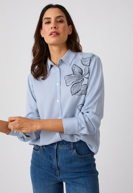 Le mannequin porte une blouse rayée bleu et blanc avec un imprimé floral noir sur la poitrine.