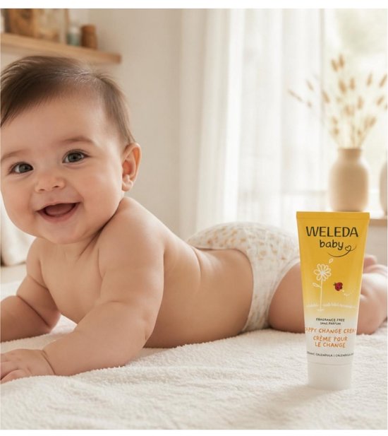 Lachende baby ligt op de buik, met een tube Weleda billenbalsem.
