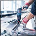 Blauwe en rode Bosch Professional boorhamer met SDS-plus boor, vastgehouden door een persoon met rode werkhandschoenen.