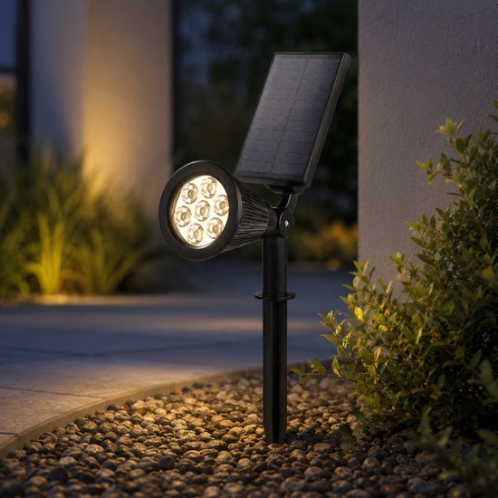 Zwarte solaire tuinspot met zeven LED's en een zonnepaneel, die warm wit licht uitstraalt op kasseien.