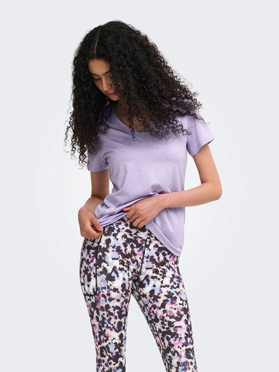Model in paars sportshirt met V-hals en een veelkleurige legging met abstracte print. Ze trekt aan haar shirt.
