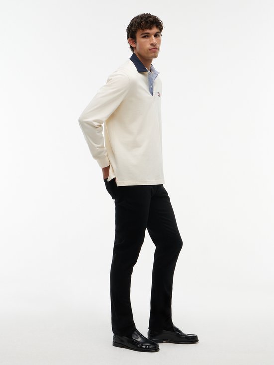 Model draagt een zwarte spijkerbroek van Tommy Jeans met een beige poloshirt.