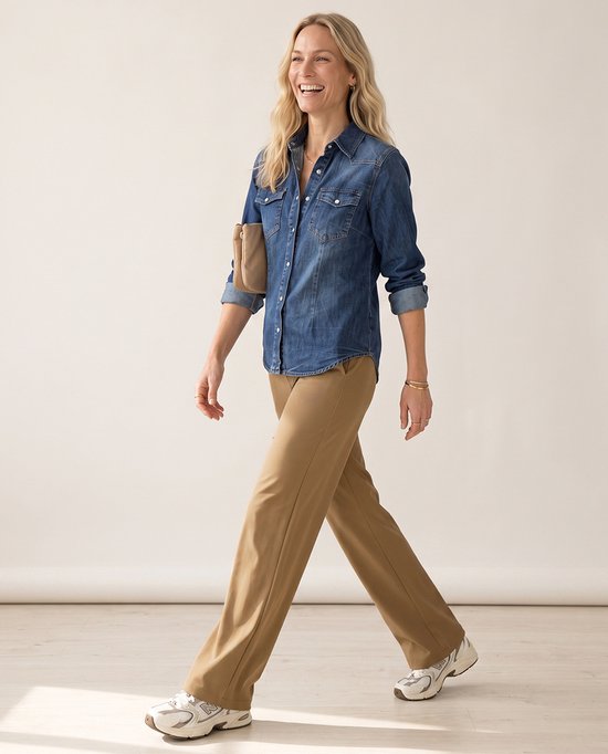 Model in jeansblouse en bruine travelstof broek met rechte pijpen en witte sneakers.