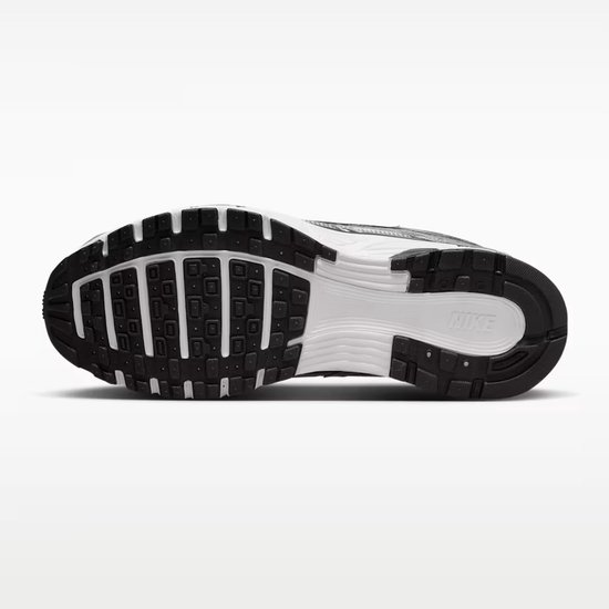 Onderkant van een grijze Nike P-6000 sneaker. Zwarte rubberen zool met wit en grijs middenstuk. 'NIKE' op de hiel.