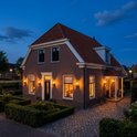 Buitenlampen aan een bakstenen huis, verlichten de voortuin en oprit bij avond.