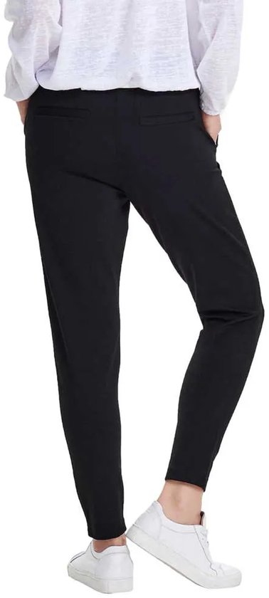 Achterkant van een vrouw in een zwarte chino met wijde pijpen en witte sneakers.