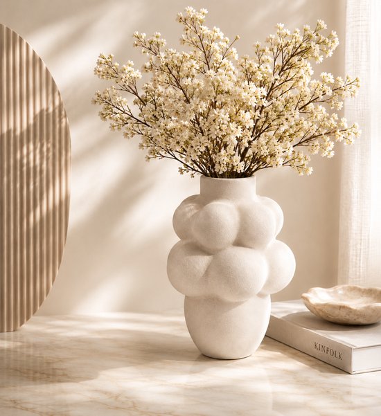 Vase en céramique blanc crème à design bullé, rempli de délicates branches de fleurs blanches.