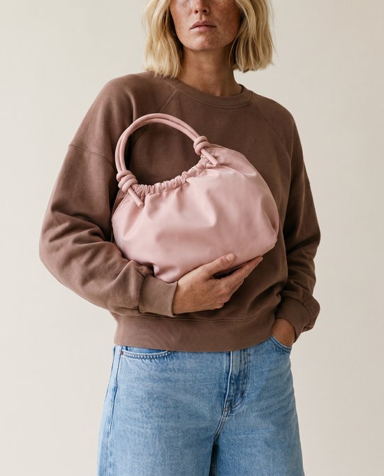 Model met lichtroze handtas met gedraaide handvatten en een losse stof.